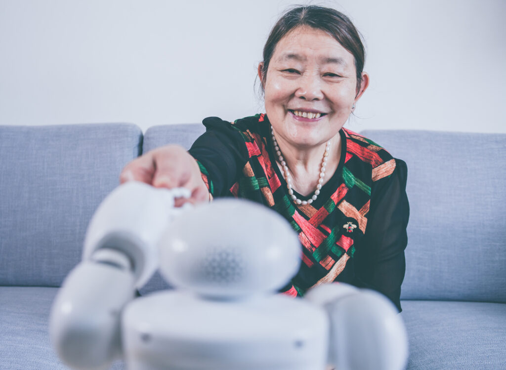 Senior woman touching robot finger indoors